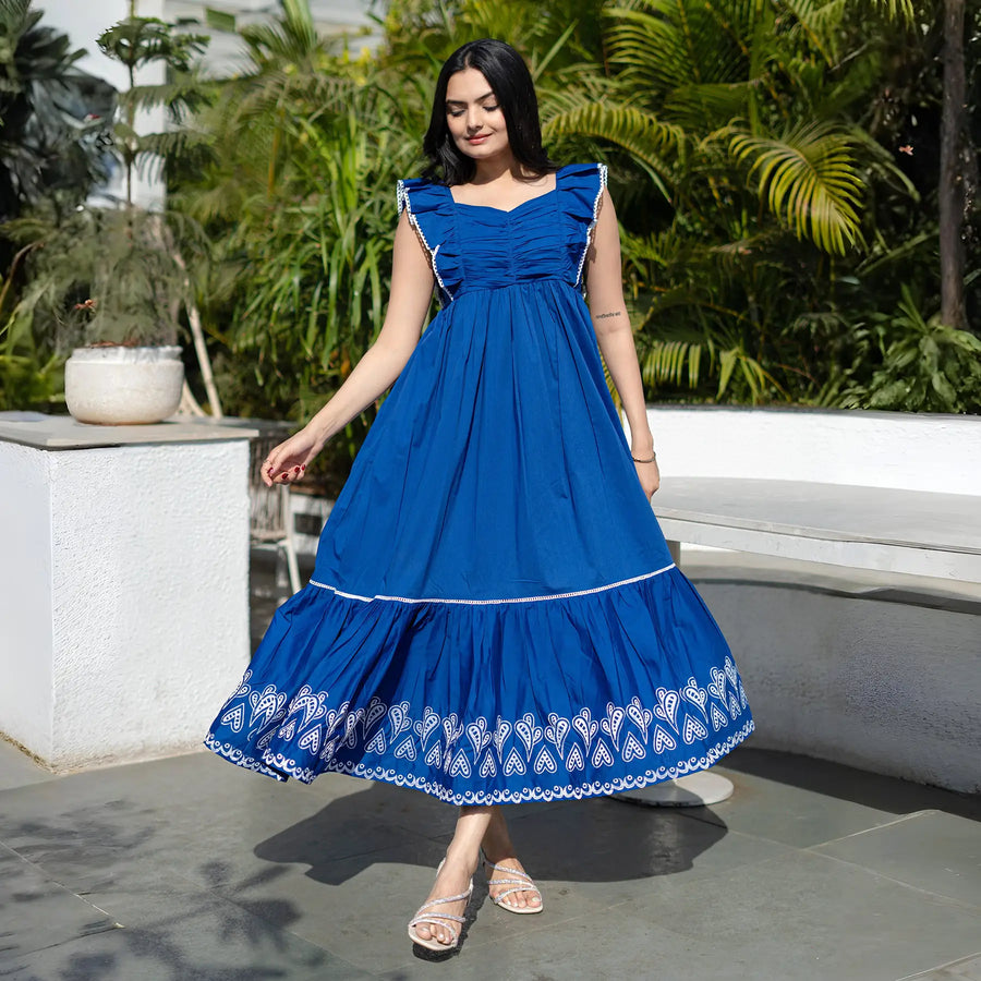Woman in a royal blue sleeveless frock dress with white embroidery at the hem.